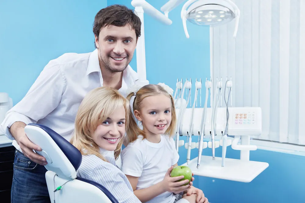 Husband, wife, and child smiling while sitting on a dental chair.